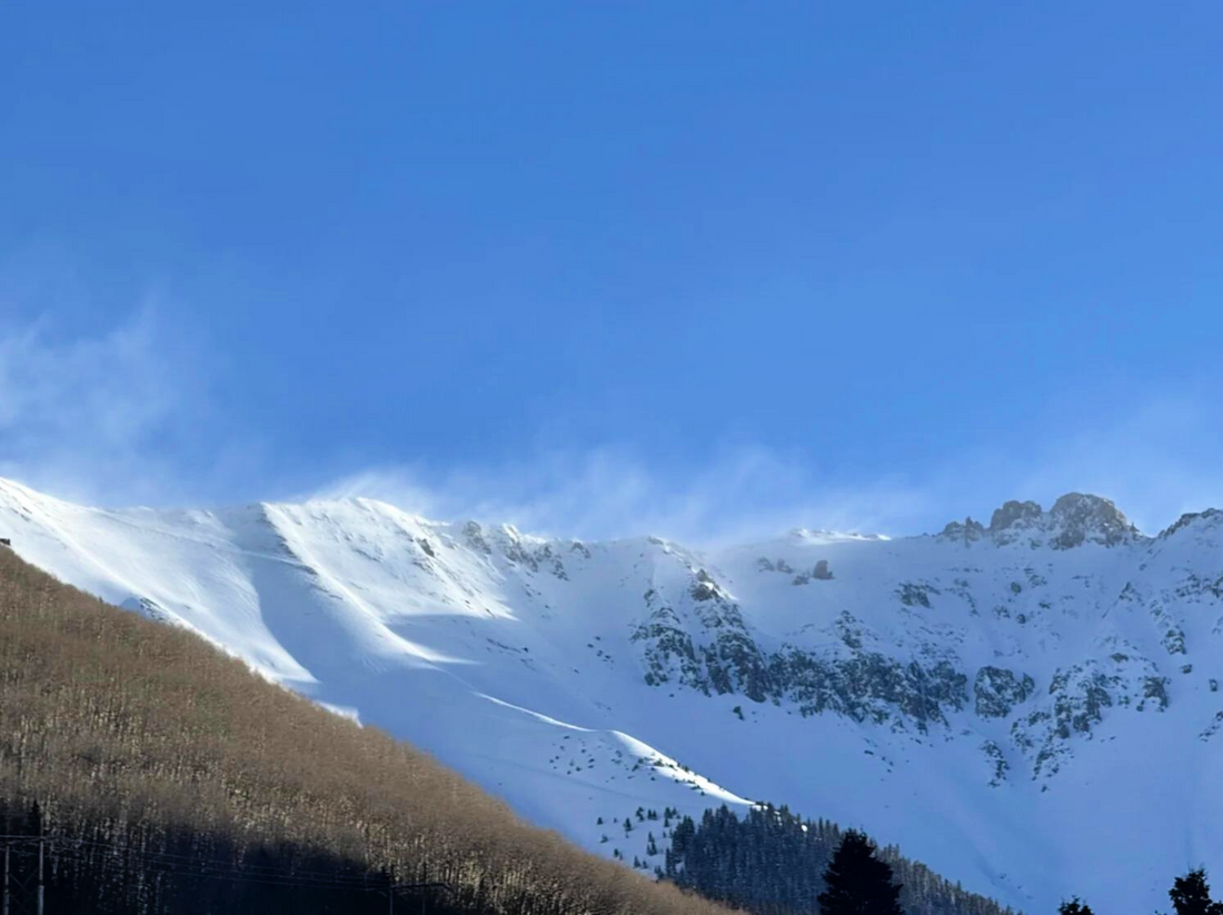 Plumes of snow or flagging on the ridgeline indicate snow is being blown from the left to the right side of the picture. The wind is drifting snow onto all the slopes in this picture.